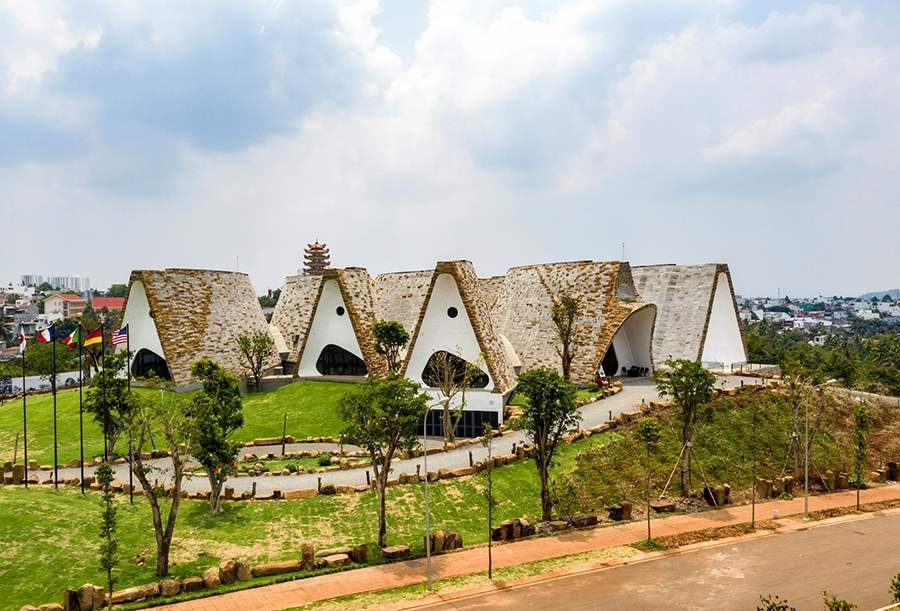 Tòa nhà có kiến trúc độc đáo với mái nhọn, nằm giữa khu vực có nhiều cây xanh và đường đi bộ.