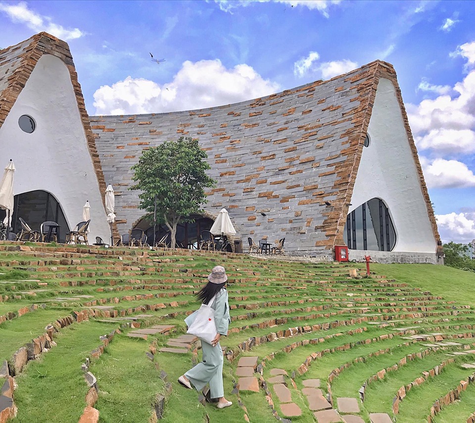 Một người đi tr&ecirc;n bậc thang cỏ trước t&ograve;a nh&agrave; c&oacute; kiến tr&uacute;c độc đ&aacute;o với m&aacute;i v&ograve;m v&agrave; tường đ&aacute;.