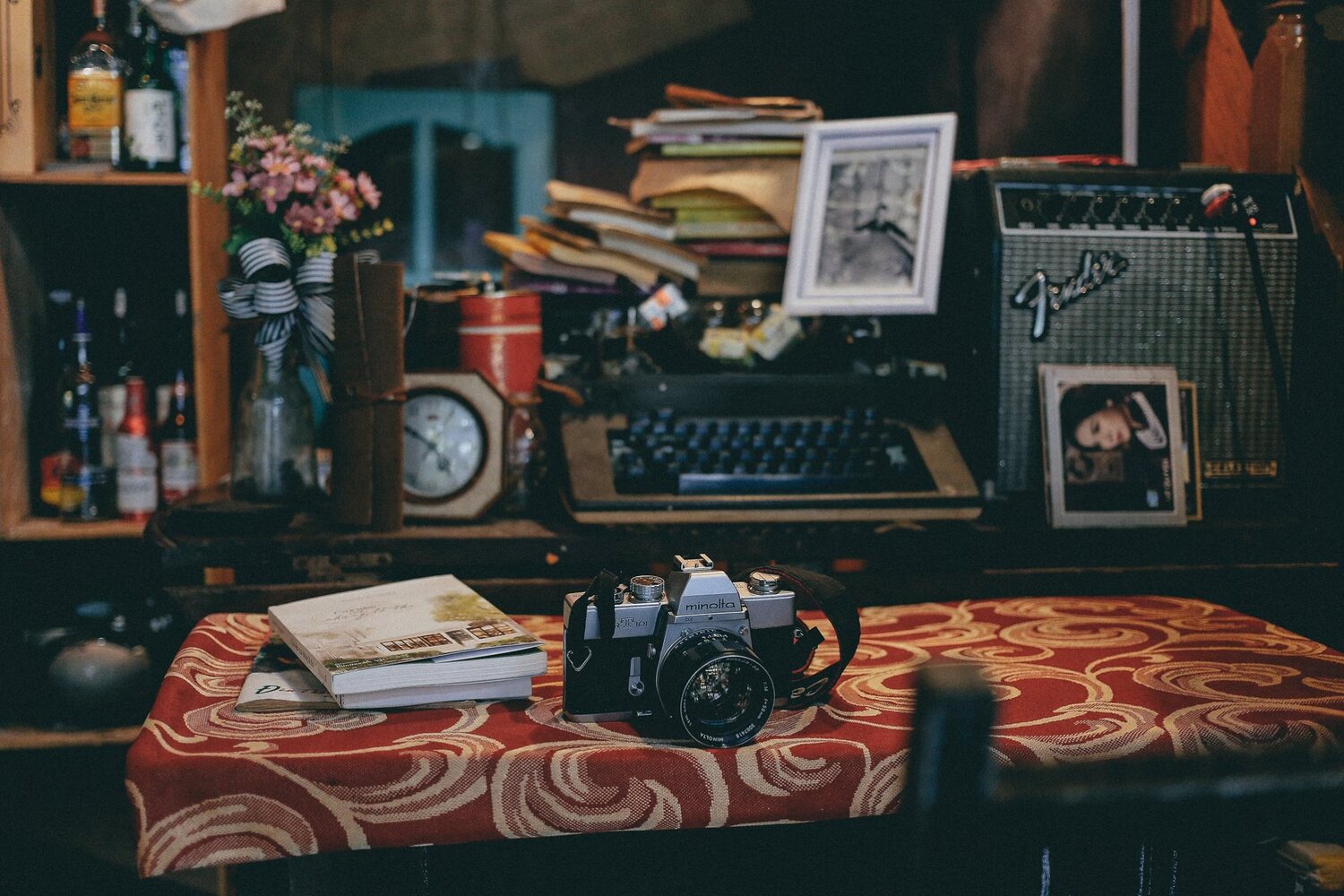 M&aacute;y ảnh cổ điển tr&ecirc;n b&agrave;n phủ khăn đỏ, b&ecirc;n cạnh s&aacute;ch, m&aacute;y đ&aacute;nh chữ, v&agrave; ảnh trong kh&ocirc;ng gian ấm c&uacute;ng.