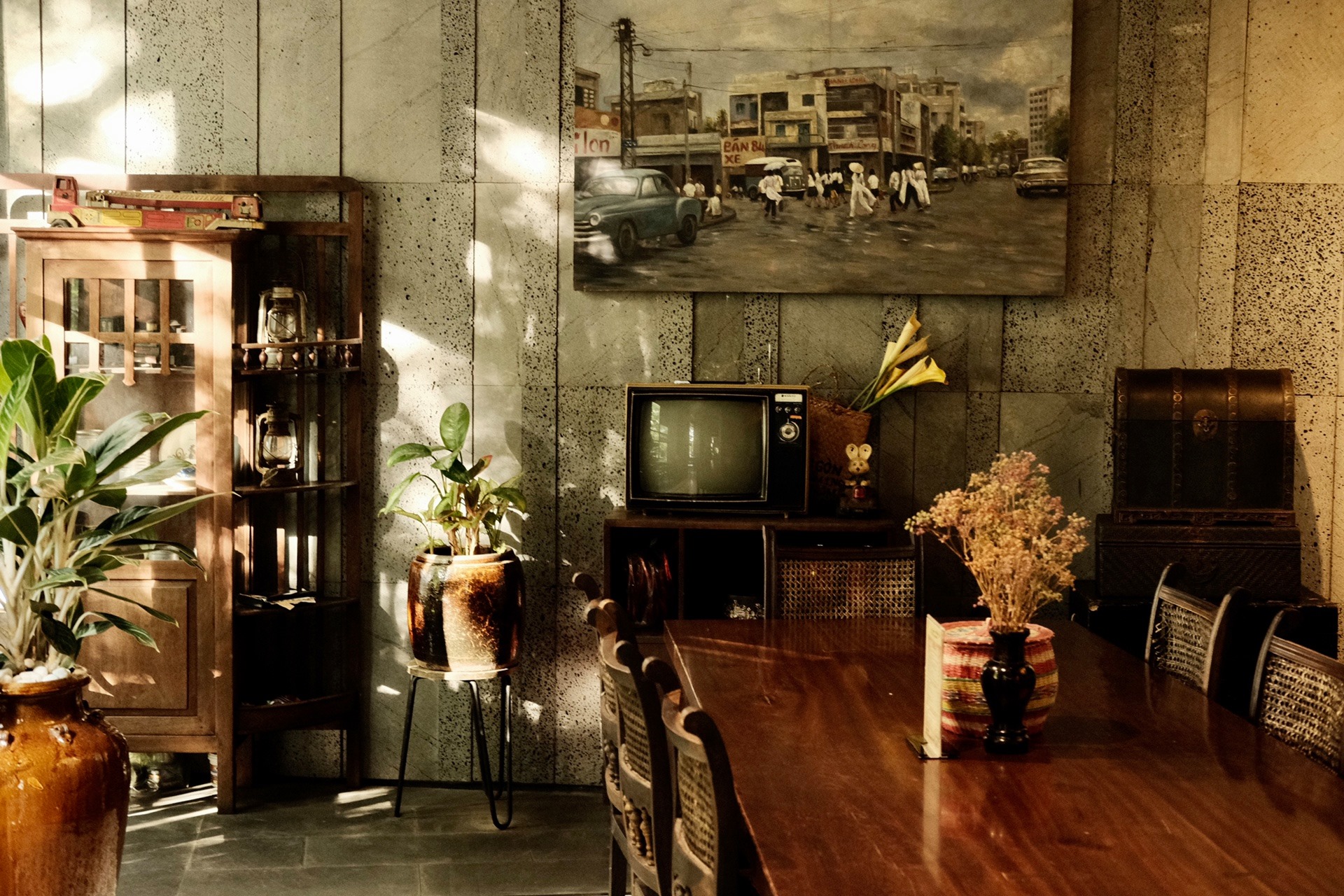 Ph&ograve;ng kh&aacute;ch cổ điển với tivi cũ, tranh tường, b&agrave;n ghế gỗ, c&acirc;y cảnh v&agrave; &aacute;nh s&aacute;ng tự nhi&ecirc;n chiếu v&agrave;o.