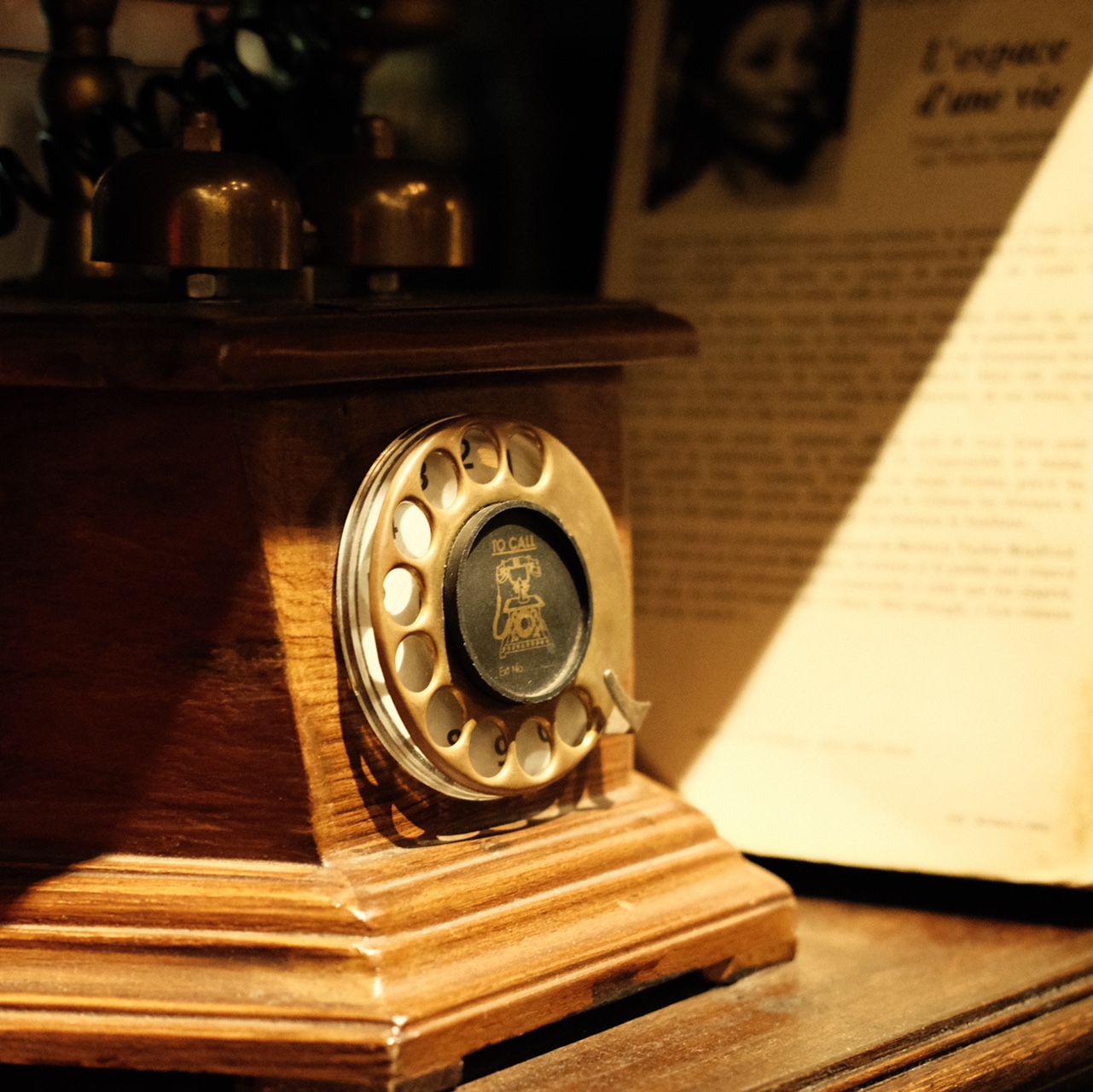 Điện thoại quay số cổ điển bằng gỗ, b&ecirc;n cạnh l&agrave; một trang s&aacute;ch in chữ.