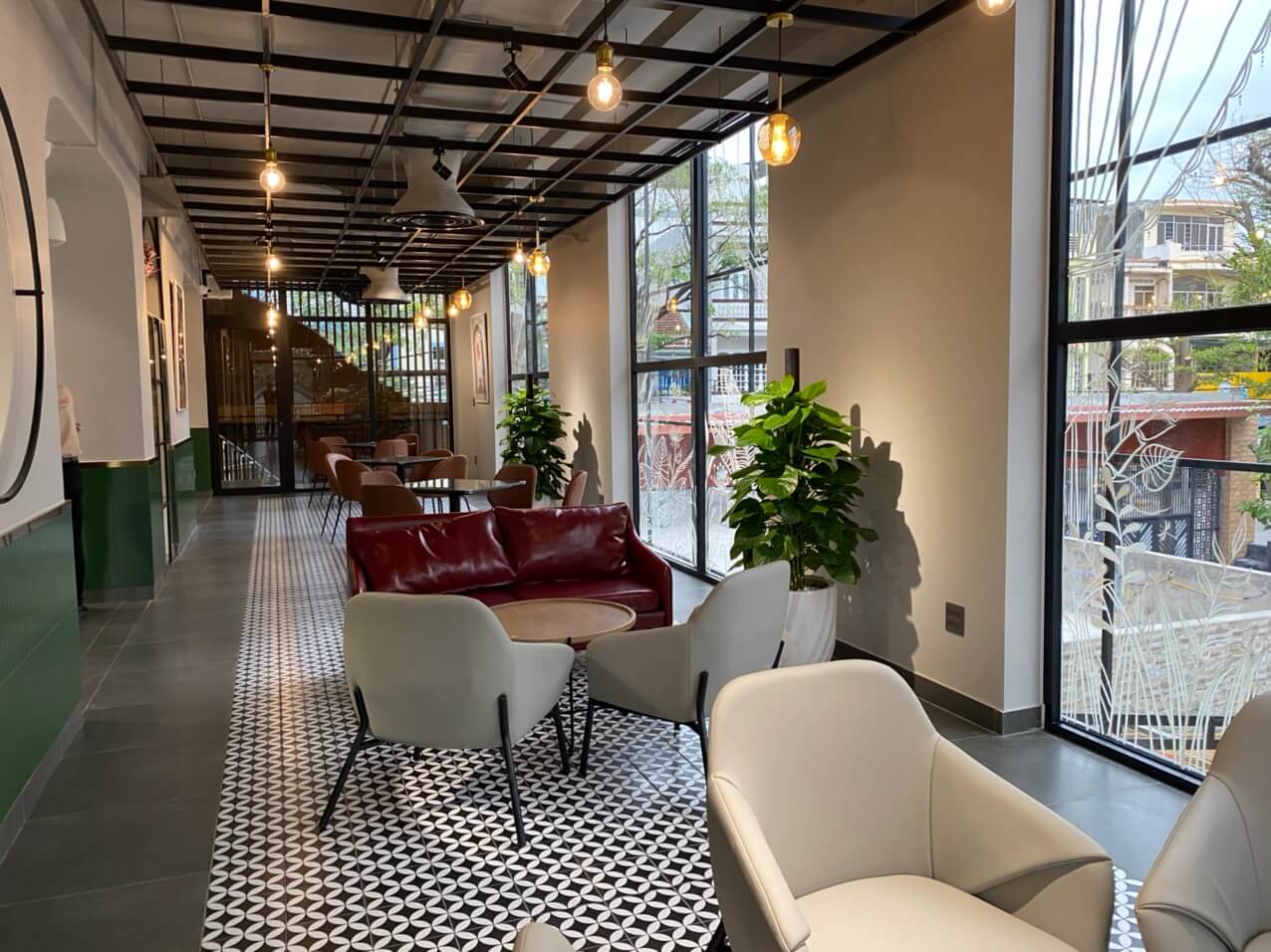 Kh&ocirc;ng gian qu&aacute;n c&agrave; ph&ecirc; hiện đại với ghế sofa đỏ, b&agrave;n gỗ v&agrave; cửa sổ lớn nh&igrave;n ra b&ecirc;n ngo&agrave;i.