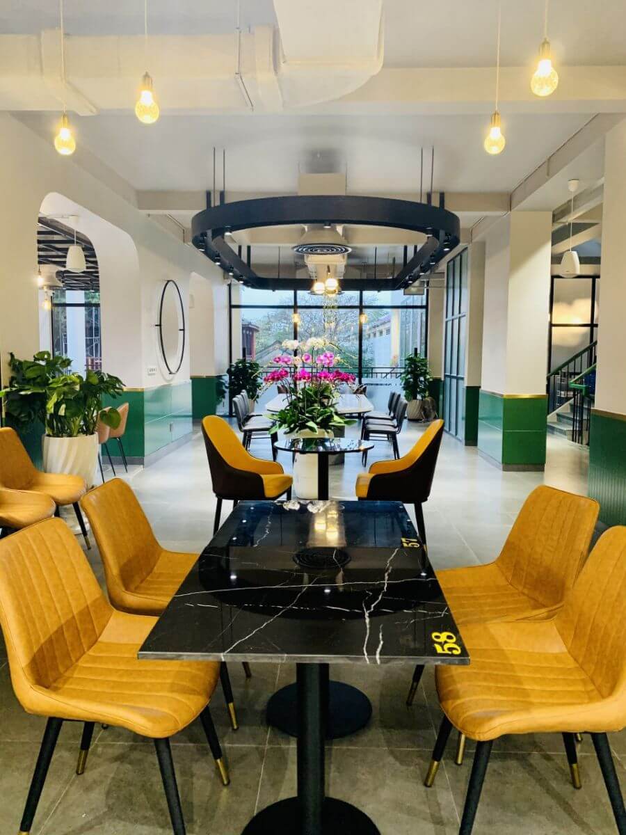 Kh&ocirc;ng gian nh&agrave; h&agrave;ng hiện đại với b&agrave;n ghế m&agrave;u v&agrave;ng, c&acirc;y xanh trang tr&iacute; v&agrave; đ&egrave;n trần s&aacute;ng tạo.