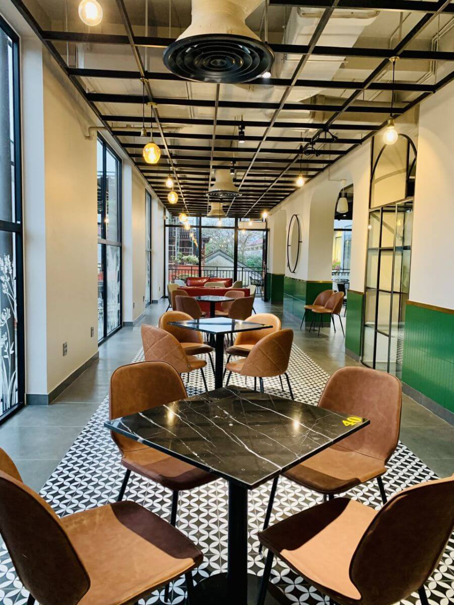 Qu&aacute;n c&agrave; ph&ecirc; hiện đại với b&agrave;n ghế gỗ, trần đ&egrave;n treo v&agrave; cửa sổ k&iacute;nh lớn, tạo kh&ocirc;ng gian tho&aacute;ng đ&atilde;ng v&agrave; sang trọng.