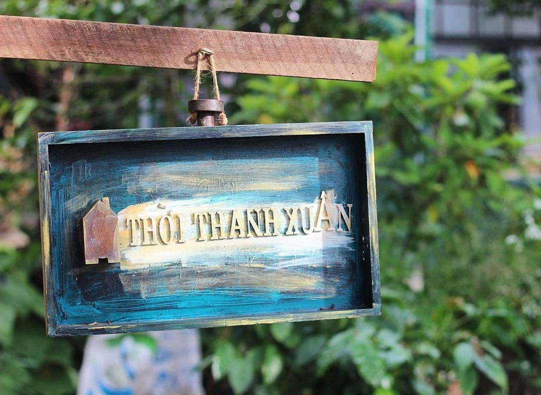 Biển hiệu gỗ với d&ograve;ng chữ "Thời Thanh Xu&acirc;n" treo tr&ecirc;n nền c&acirc;y xanh ph&iacute;a sau.