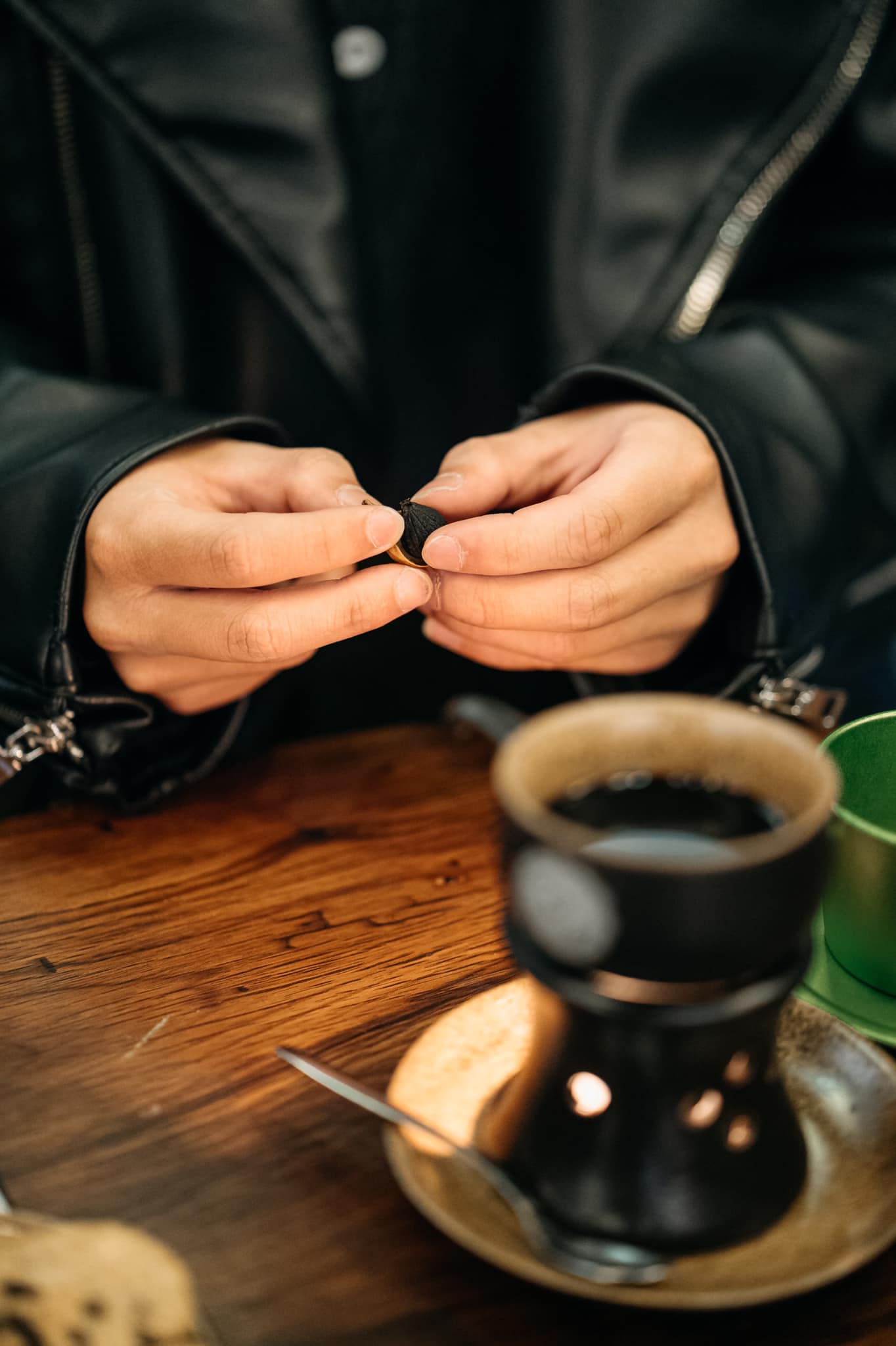 Đôi tay đang cầm một vật nhỏ màu đen, bên cạnh là một ly cà phê trên bàn gỗ.