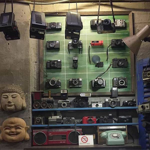 Bức tường trưng b&agrave;y đầy m&aacute;y ảnh cổ, k&egrave;m theo tượng v&agrave; c&aacute;c đồ vật cổ điển kh&aacute;c, tạo cảm gi&aacute;c ho&agrave;i cổ.