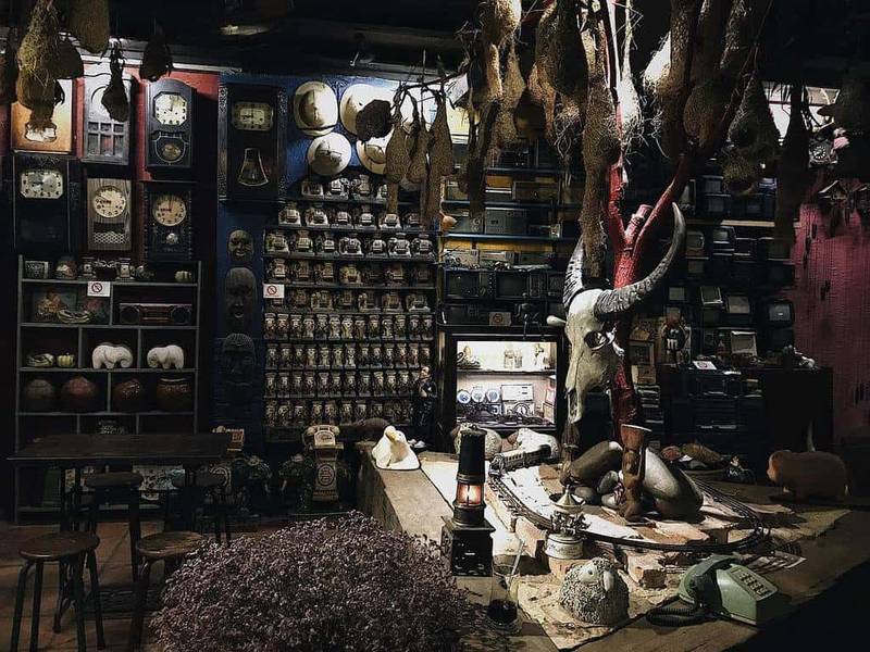 G&oacute;c ph&ograve;ng trưng b&agrave;y với nhiều đồng hồ cổ, đầu l&acirc;u, v&agrave; c&aacute;c vật trang tr&iacute; độc đ&aacute;o, &aacute;nh s&aacute;ng mờ ảo.