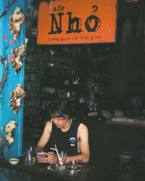 Người ngồi trong qu&aacute;n c&agrave; ph&ecirc; trang tr&iacute; cổ điển, sử dụng điện thoại dưới biển hiệu "Cafe Nhỏ".