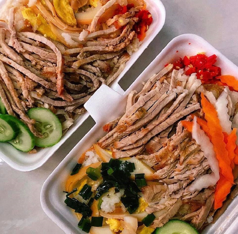 Hai phần cơm tấm với thịt cắt l&aacute;t, dưa leo v&agrave; đồ chua, được b&agrave;y tr&ecirc;n hộp xốp m&agrave;u trắng.