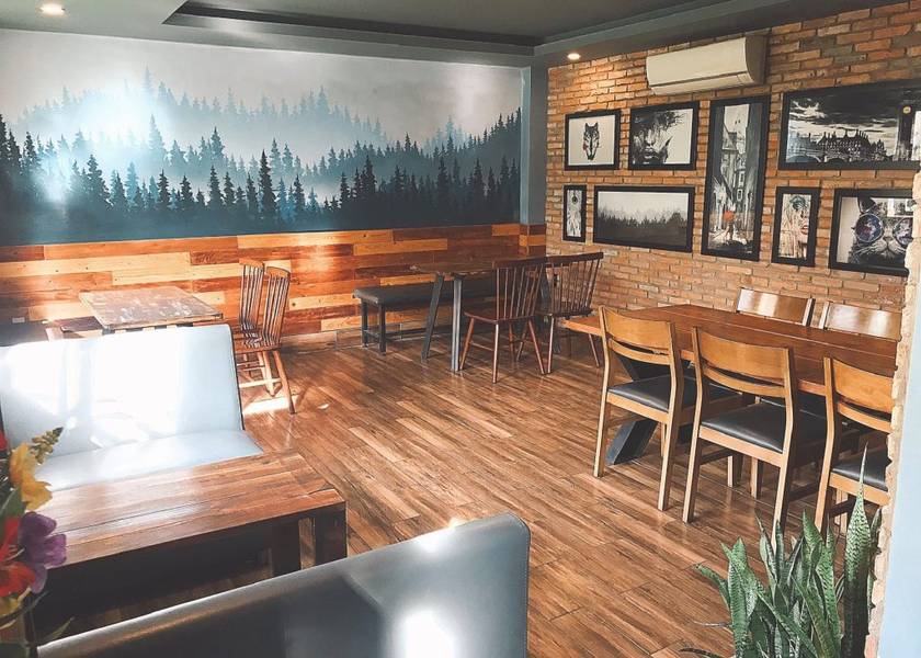 Qu&aacute;n c&agrave; ph&ecirc; với nội thất gỗ, tranh tường rừng c&acirc;y, b&agrave;n ghế gỗ v&agrave; tường gạch trang tr&iacute; h&igrave;nh ảnh nghệ thuật.