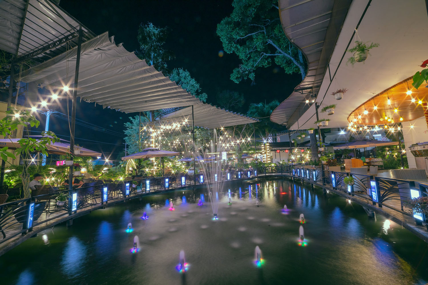 Khu vực s&acirc;n vườn buổi tối với đ&egrave;n trang tr&iacute; lấp l&aacute;nh, hồ nước v&agrave; đ&agrave;i phun nước m&agrave;u sắc, kh&ocirc;ng gian thư gi&atilde;n.