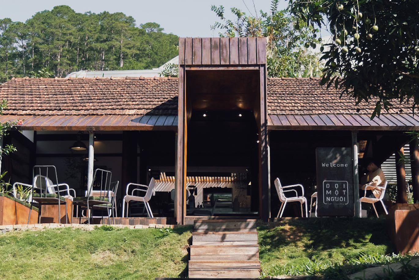 Qu&aacute;n c&agrave; ph&ecirc; với thiết kế gỗ, m&aacute;i ng&oacute;i đỏ, c&oacute; b&agrave;n ghế ngo&agrave;i trời v&agrave; c&acirc;y xanh xung quanh.