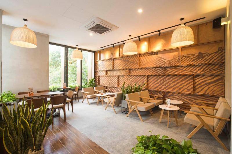 Qu&aacute;n c&agrave; ph&ecirc; với thiết kế nội thất ấm c&uacute;ng, c&oacute; b&agrave;n ghế gỗ, đ&egrave;n treo v&agrave; c&acirc;y xanh trang tr&iacute;.