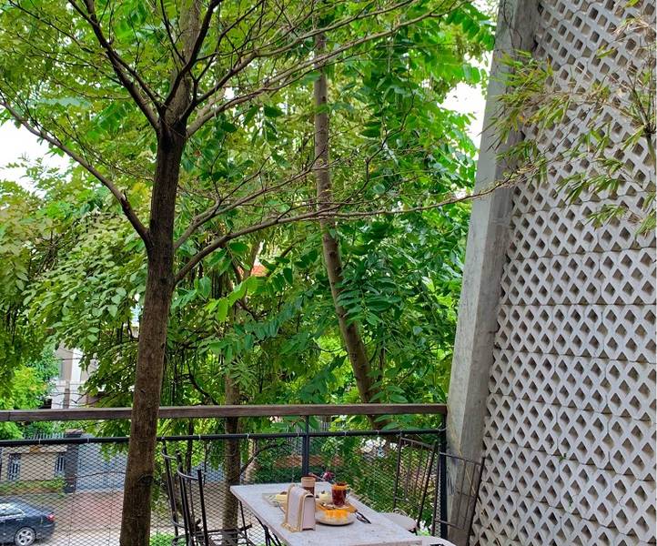 B&agrave;n ngo&agrave;i trời với đồ ăn v&agrave; đồ uống, xung quanh l&agrave; c&acirc;y xanh v&agrave; h&agrave;ng r&agrave;o, gần một bức tường c&oacute; hoa văn.