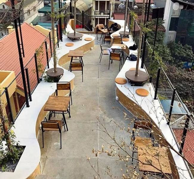 S&acirc;n thượng qu&aacute;n c&agrave; ph&ecirc; với b&agrave;n ghế gỗ, c&acirc;y xanh v&agrave; m&aacute;i hi&ecirc;n đỏ, tạo kh&ocirc;ng gian tho&aacute;ng đ&atilde;ng v&agrave; thư gi&atilde;n.