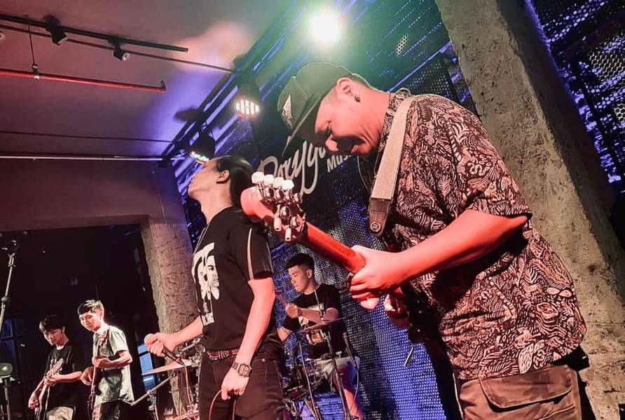 Ban nhạc đang biểu diễn tr&ecirc;n s&acirc;n khấu, với &aacute;nh s&aacute;ng sắc m&agrave;u v&agrave; c&aacute;c nhạc cụ như guitar v&agrave; trống.