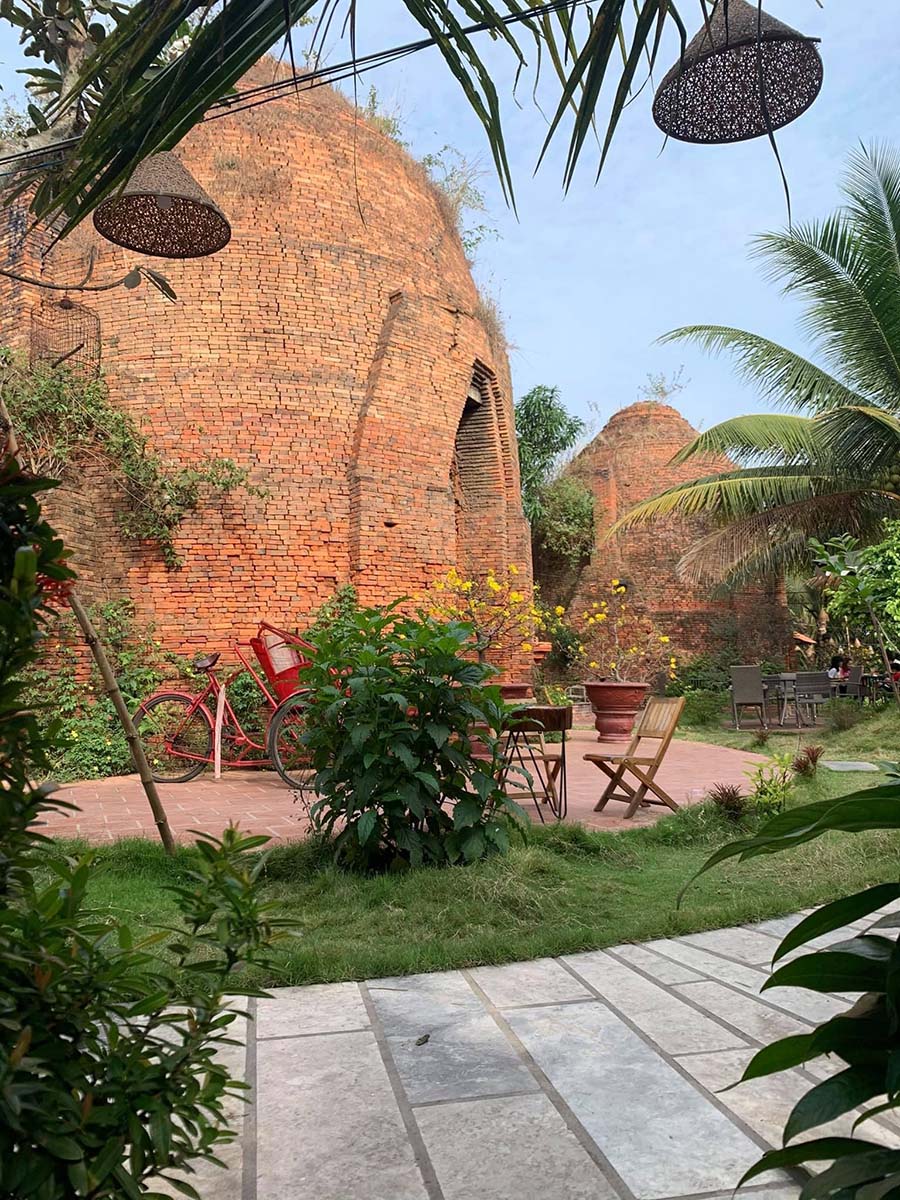 Khu vườn với l&ograve; gạch cổ, xe đạp đỏ v&agrave; b&agrave;n ghế gỗ, xung quanh l&agrave; c&acirc;y xanh tươi tốt.