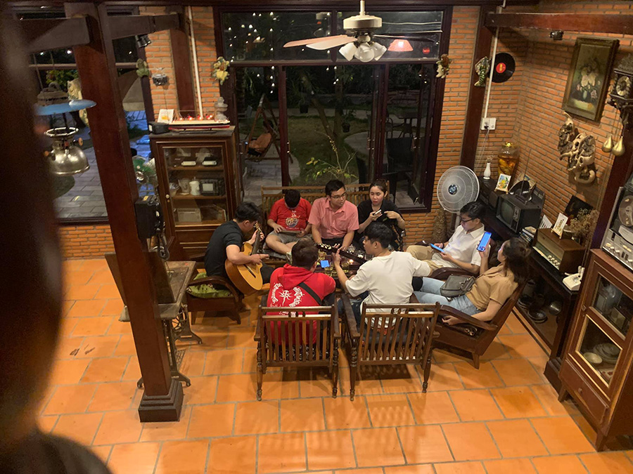 Một nh&oacute;m người ngồi tr&ograve; chuyện v&agrave; chơi guitar trong một căn ph&ograve;ng ấm c&uacute;ng với nội thất bằng gỗ.