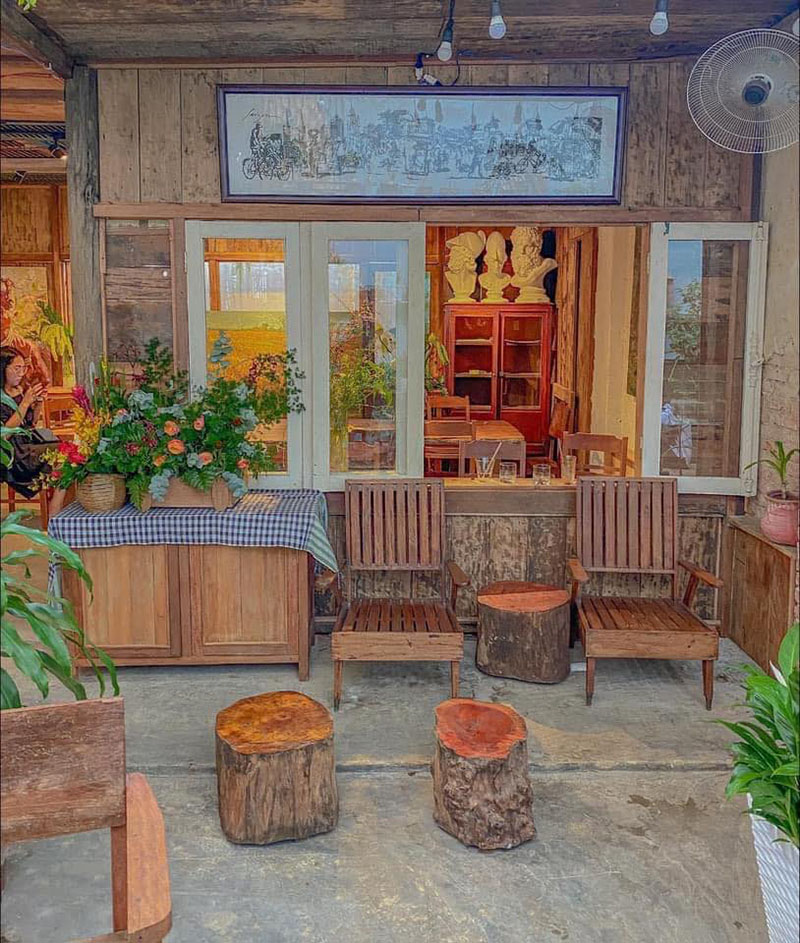 Qu&aacute;n c&agrave; ph&ecirc; phong c&aacute;ch vintage với b&agrave;n ghế gỗ, tranh treo tường v&agrave; b&igrave;nh hoa trang tr&iacute;, tạo cảm gi&aacute;c ấm c&uacute;ng.