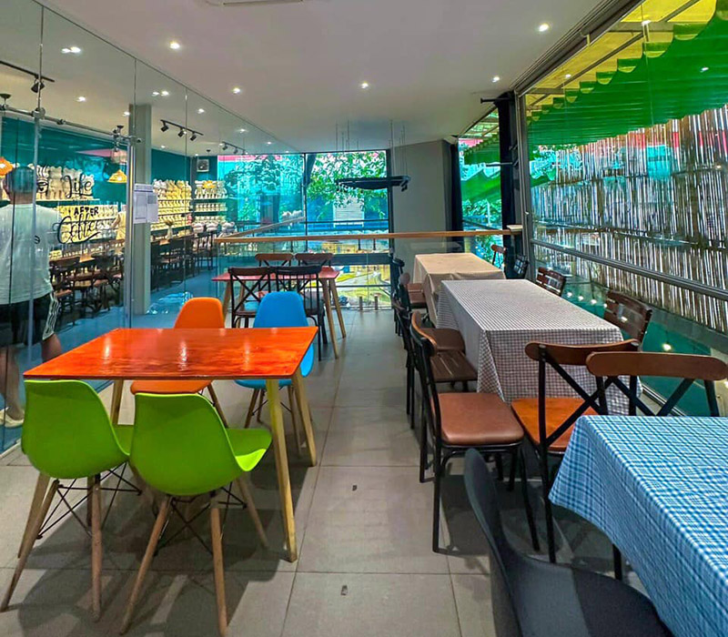 Qu&aacute;n c&agrave; ph&ecirc; với b&agrave;n ghế đa sắc, kh&ocirc;ng gian s&aacute;ng sủa, cửa k&iacute;nh lớn nh&igrave;n ra cảnh ngo&agrave;i trời.