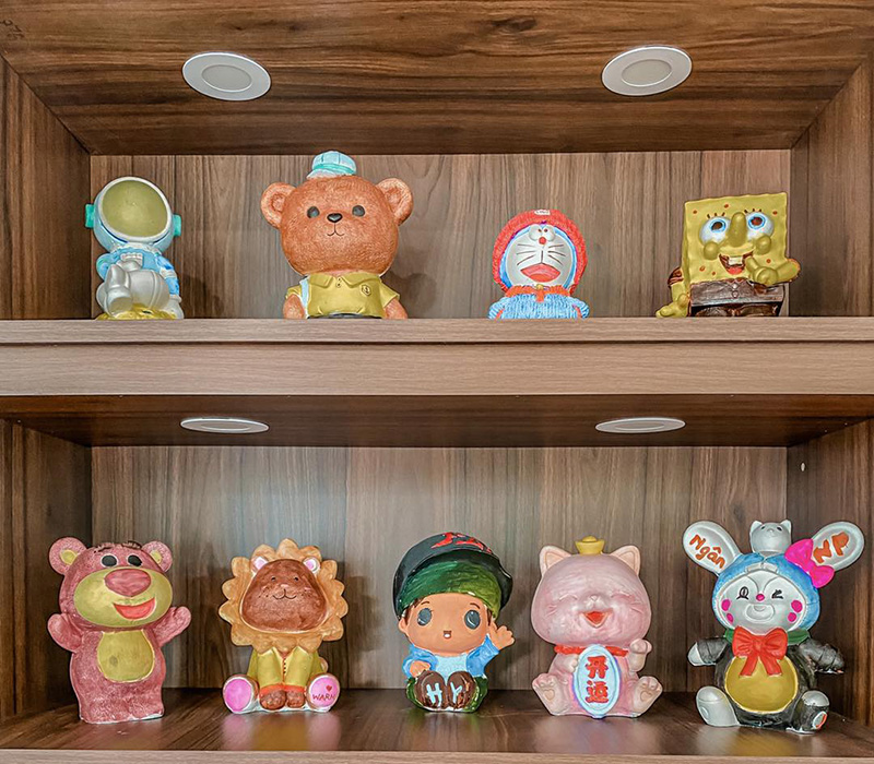 C&aacute;c tượng nh&acirc;n vật hoạt h&igrave;nh đầy m&agrave;u sắc được trưng b&agrave;y tr&ecirc;n hai kệ gỗ trong một kh&ocirc;ng gian nội thất.