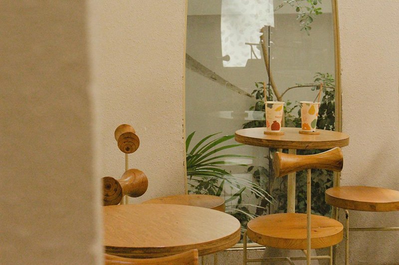 Quán cà phê trang trí hiện đại với bàn ghế gỗ, ly nước hoa quả và cây xanh trong không gian yên tĩnh.