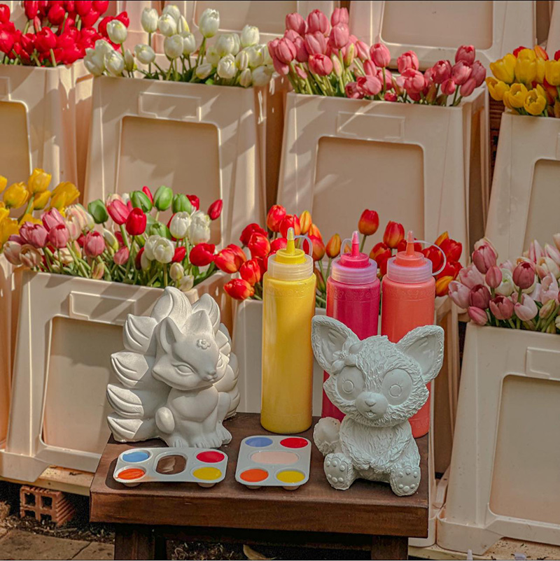 C&aacute;c b&igrave;nh hoa tulip nhiều m&agrave;u sắc ph&iacute;a sau b&agrave;n với tượng gốm trắng, bảng m&agrave;u v&agrave; chai sơn.