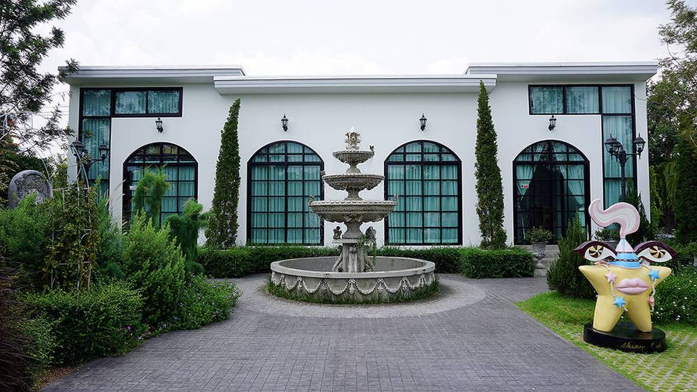 T&ograve;a nh&agrave; trắng với cửa sổ lớn, đ&agrave;i phun nước ph&iacute;a trước v&agrave; tượng trang tr&iacute; h&igrave;nh ng&ocirc;i sao b&ecirc;n phải.