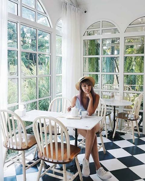 Người ngồi trong qu&aacute;n c&agrave; ph&ecirc; s&aacute;ng sủa với cửa sổ lớn v&agrave; s&agrave;n caro, xung quanh l&agrave; c&acirc;y xanh.