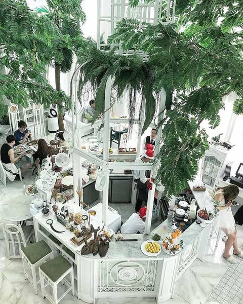 Qu&aacute;n c&agrave; ph&ecirc; với thiết kế nội thất trắng, c&acirc;y xanh treo tr&ecirc;n trần, kh&aacute;ch h&agrave;ng ngồi thưởng thức đồ uống v&agrave; tr&ograve; chuyện.