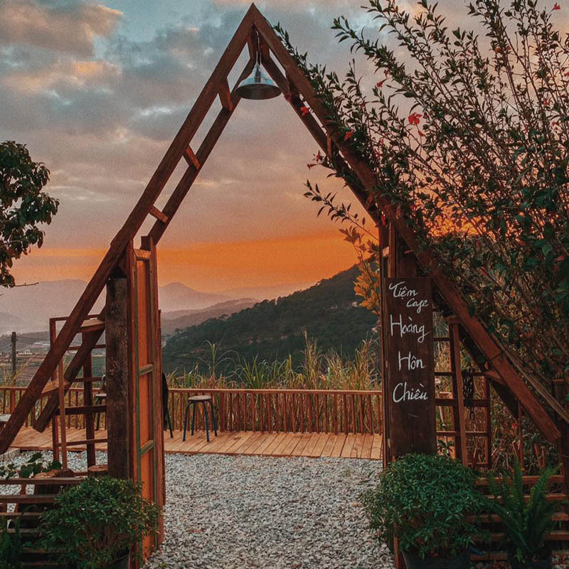 Khung cảnh ho&agrave;ng h&ocirc;n tr&ecirc;n n&uacute;i với cổng gỗ h&igrave;nh tam gi&aacute;c v&agrave; c&acirc;y cối xung quanh, tạo cảm gi&aacute;c y&ecirc;n b&igrave;nh.
