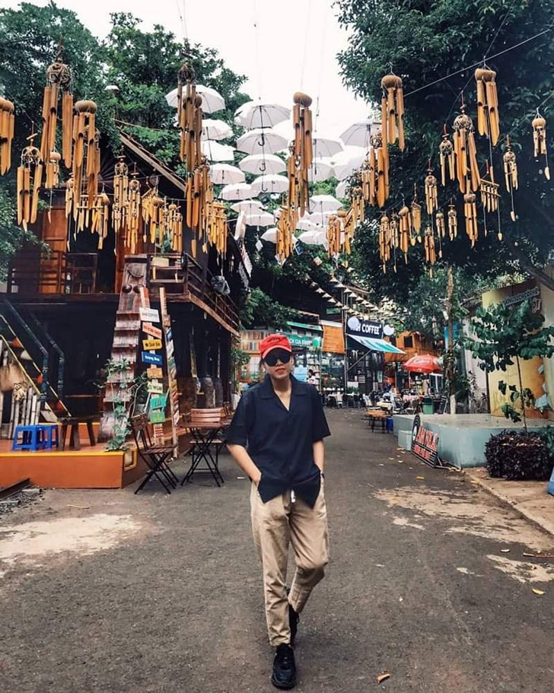 Người đàn ông đội mũ đỏ dạo phố dưới những chiếc ô và chuông gió treo trên cao.