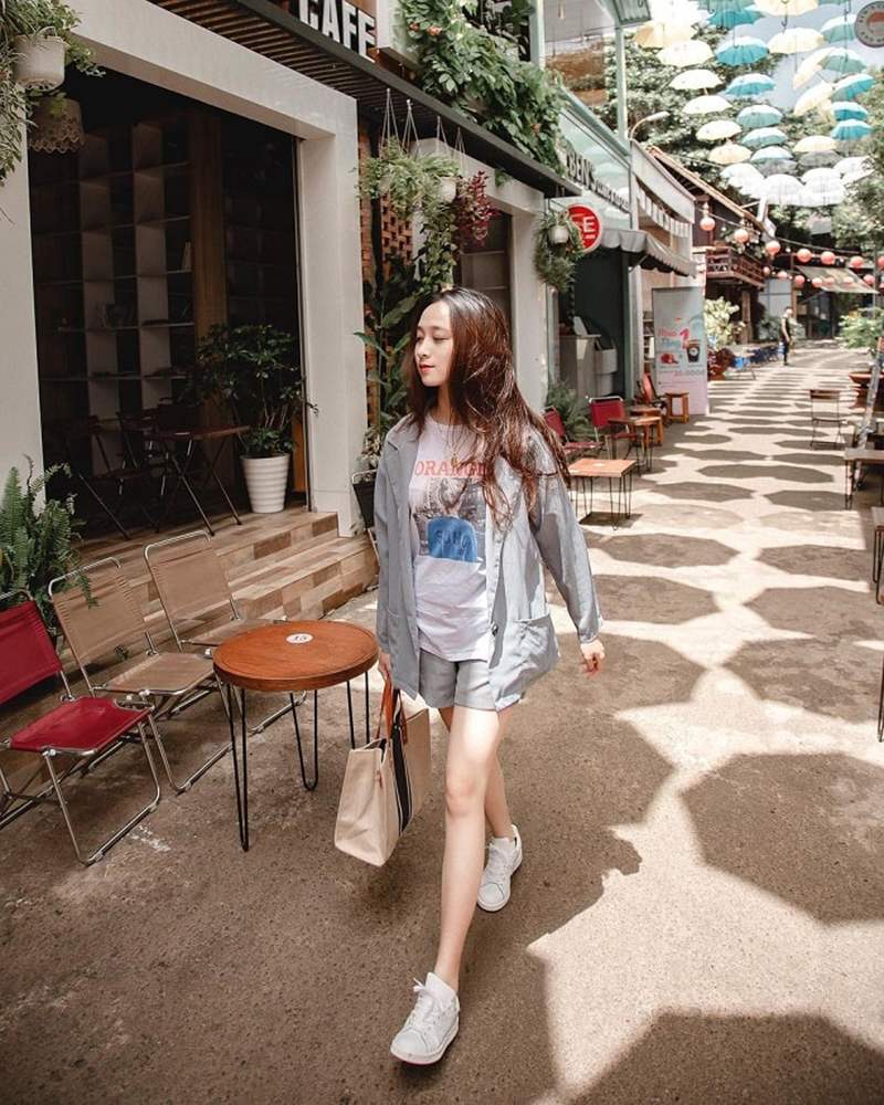 Người phụ nữ đang đi bộ trên phố với nhiều cây dù màu sắc treo phía trên, bên ngoài quán cà phê.