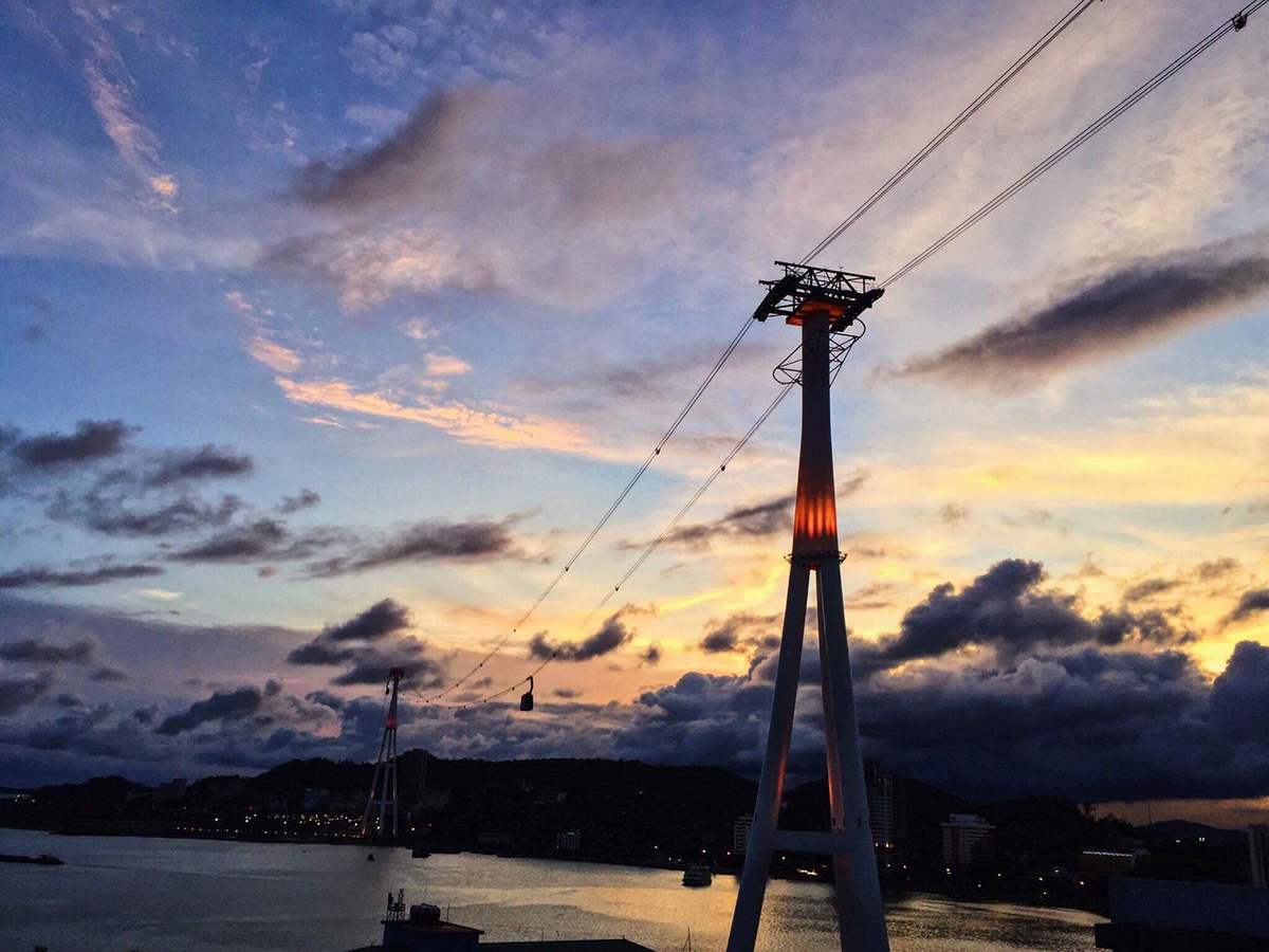 C&aacute;p treo qua s&ocirc;ng dưới bầu trời ho&agrave;ng h&ocirc;n với m&acirc;y v&agrave; &aacute;nh s&aacute;ng phản chiếu tr&ecirc;n mặt nước.