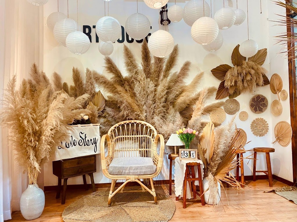Một góc trang trí với ghế mây, bình hoa, và các loại lá khô trên tường, tạo không gian ấm cúng và tự nhiên.