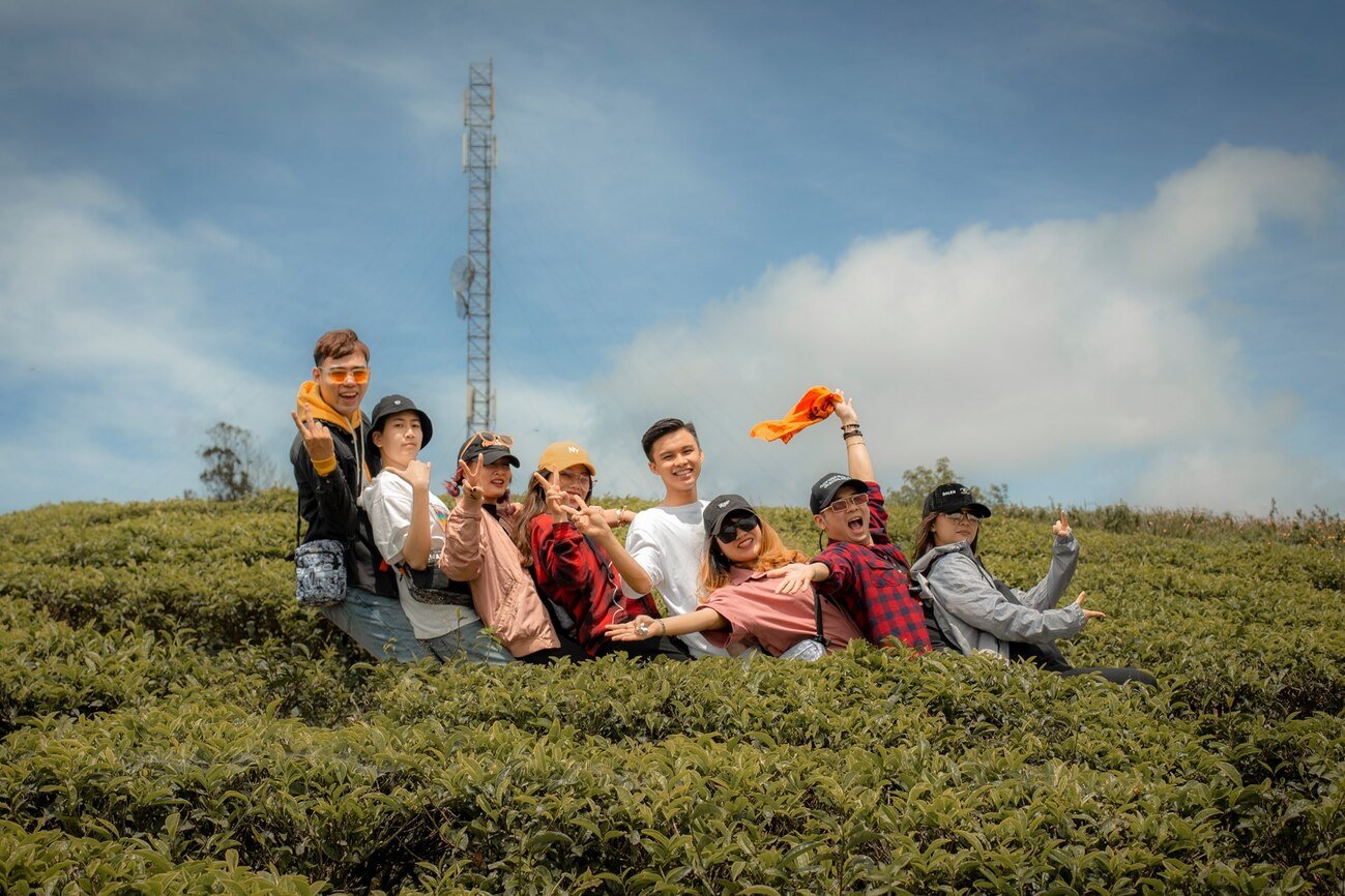 Nhóm bạn trẻ vui vẻ chụp ảnh giữa đồi chè xanh mướt dưới bầu trời xanh trong.