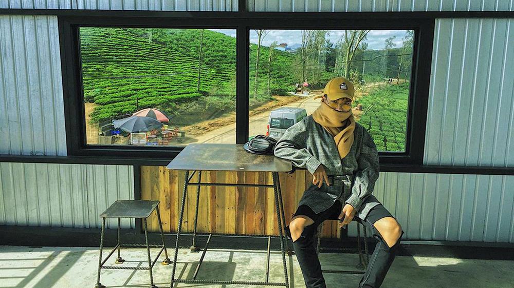 Người ngồi trong quán cà phê có cửa sổ lớn nhìn ra cánh đồng chè xanh và con đường nhỏ.