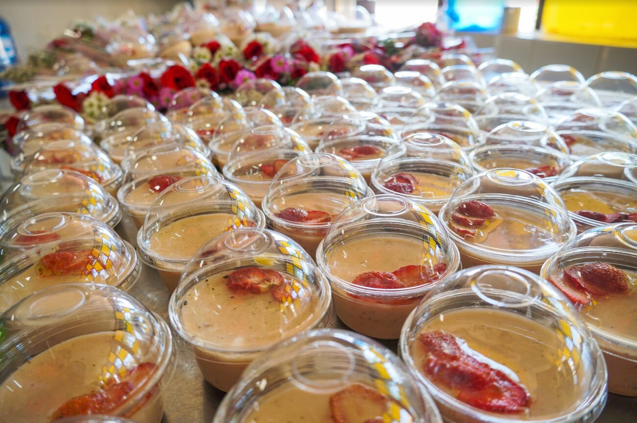 Nhiều ly nhựa có nắp đậy chứa món tráng miệng màu kem, trang trí lát dâu tây, xếp thành hàng trên bàn.