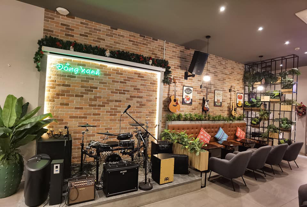 Qu&aacute;n c&agrave; ph&ecirc; với s&acirc;n khấu nhạc sống, trang tr&iacute; ghế sofa, đ&agrave;n guitar treo tường v&agrave; c&acirc;y xanh.