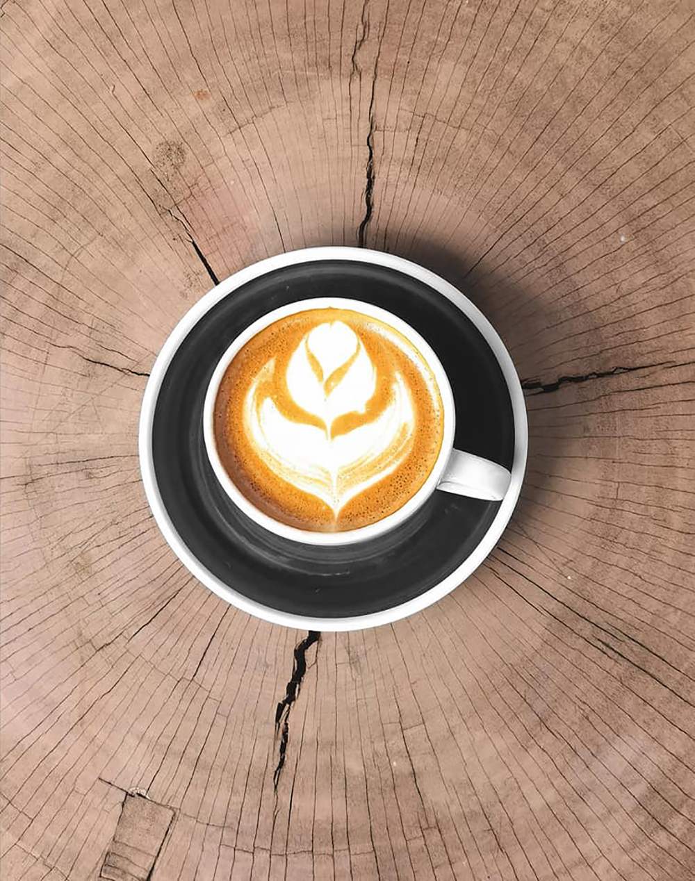 Ly c&agrave; ph&ecirc; với h&igrave;nh vẽ latte art tr&ecirc;n bề mặt, đặt tr&ecirc;n b&agrave;n gỗ c&oacute; v&acirc;n tr&ograve;n.