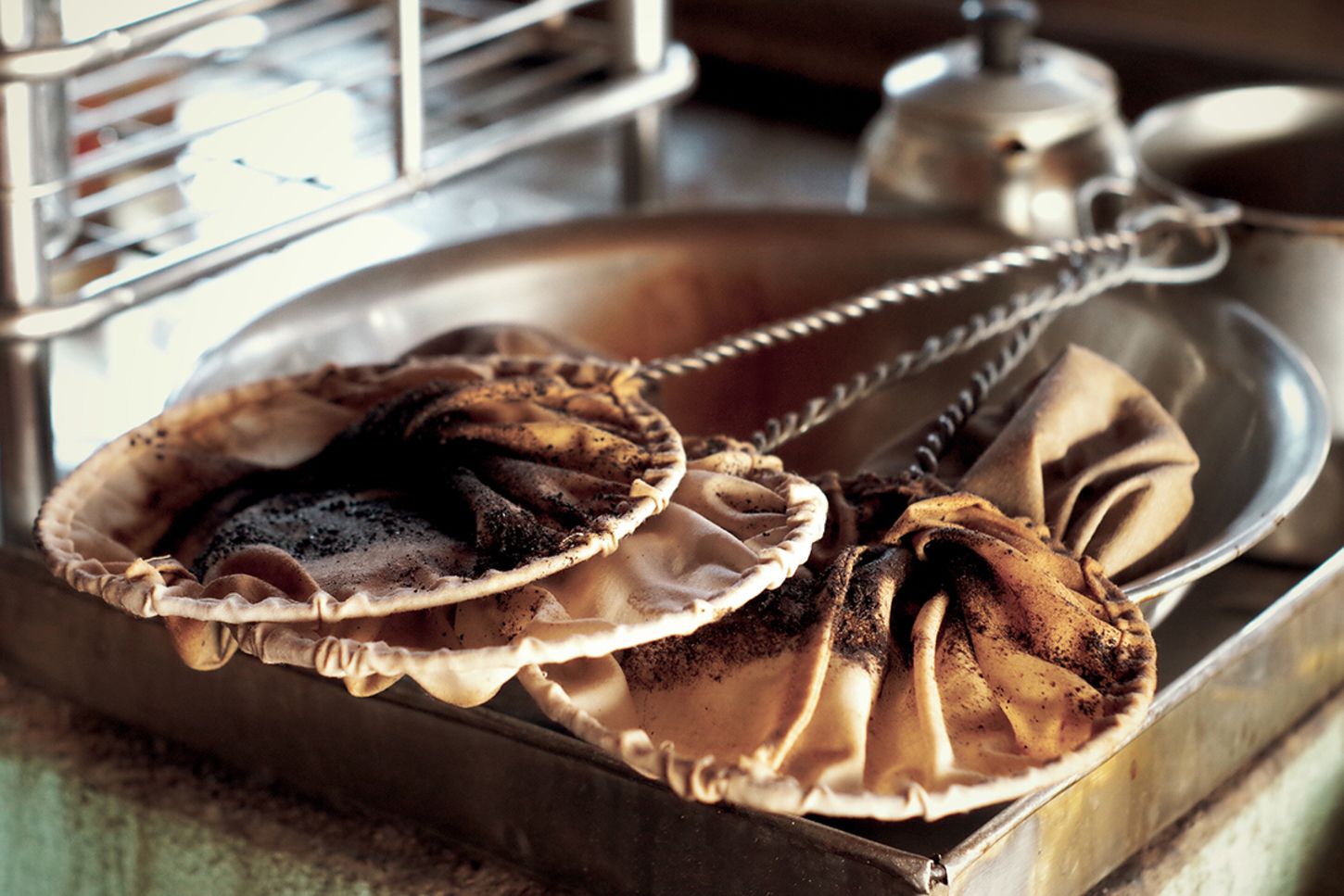 Hai bộ lọc vải chứa b&atilde; c&agrave; ph&ecirc;, đặt tr&ecirc;n khay kim loại trong kh&ocirc;ng gian nh&agrave; bếp.