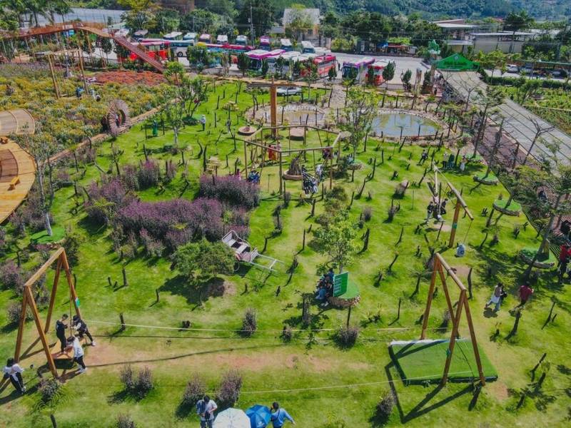 Khu vườn rộng lớn với cỏ xanh, c&acirc;y cối v&agrave; c&aacute;c tr&ograve; chơi ngo&agrave;i trời, c&oacute; nhiều người tham quan v&agrave; vui chơi.