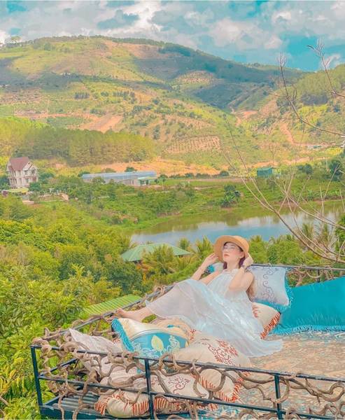 Người phụ nữ ngồi thư gi&atilde;n tr&ecirc;n ghế ngo&agrave;i trời, nh&igrave;n ra khung cảnh n&uacute;i đồi xanh tươi dưới bầu trời trong l&agrave;nh.