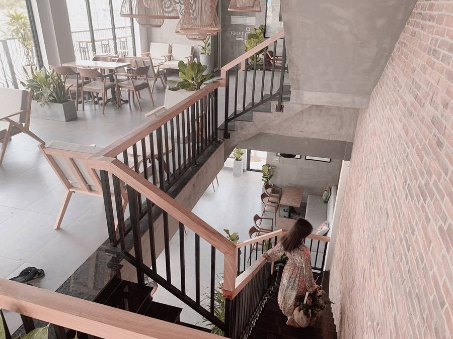 Người đi xuống cầu thang trong quán cà phê với nội thất hiện đại, ánh sáng tự nhiên và cây xanh trang trí.