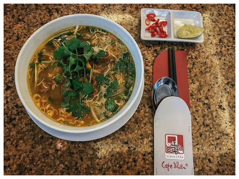 B&aacute;t phở b&ograve; với rau thơm, b&ecirc;n cạnh l&agrave; ớt v&agrave; chanh, đũa v&agrave; th&igrave;a đặt tr&ecirc;n b&agrave;n đ&aacute; hoa cương.