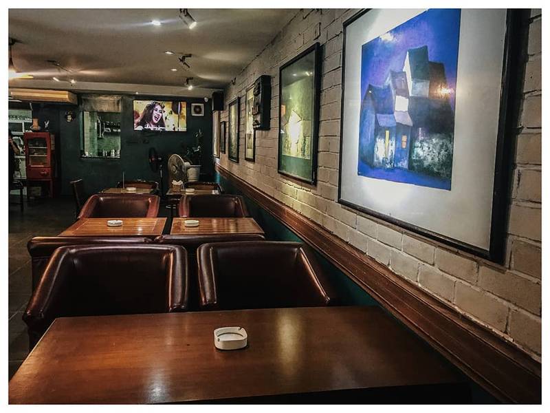 Qu&aacute;n c&agrave; ph&ecirc; với b&agrave;n ghế gỗ, tranh treo tr&ecirc;n tường gạch trắng v&agrave; m&agrave;n h&igrave;nh đang ph&aacute;t chương tr&igrave;nh truyền h&igrave;nh.