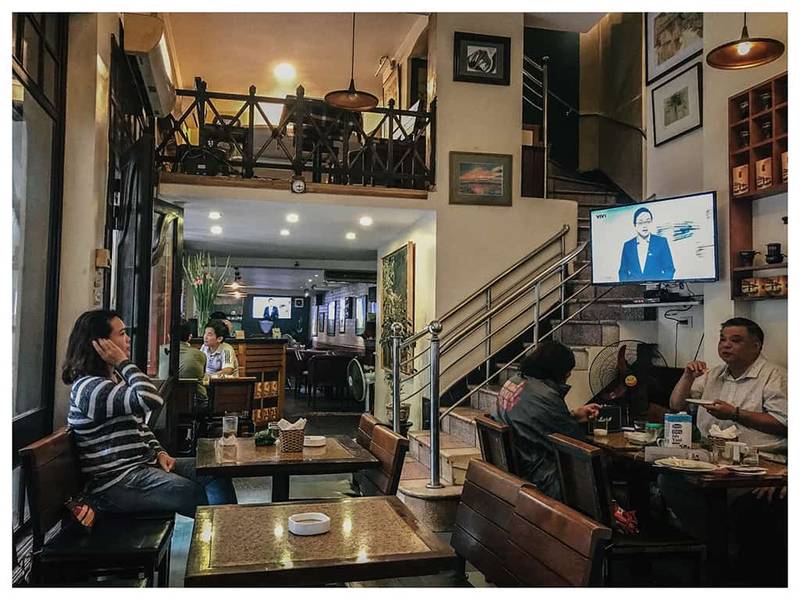 Qu&aacute;n c&agrave; ph&ecirc; ấm c&uacute;ng với v&agrave;i người ngồi tr&ograve; chuyện, xem TV, nội thất gỗ, cầu thang l&ecirc;n tầng lửng.