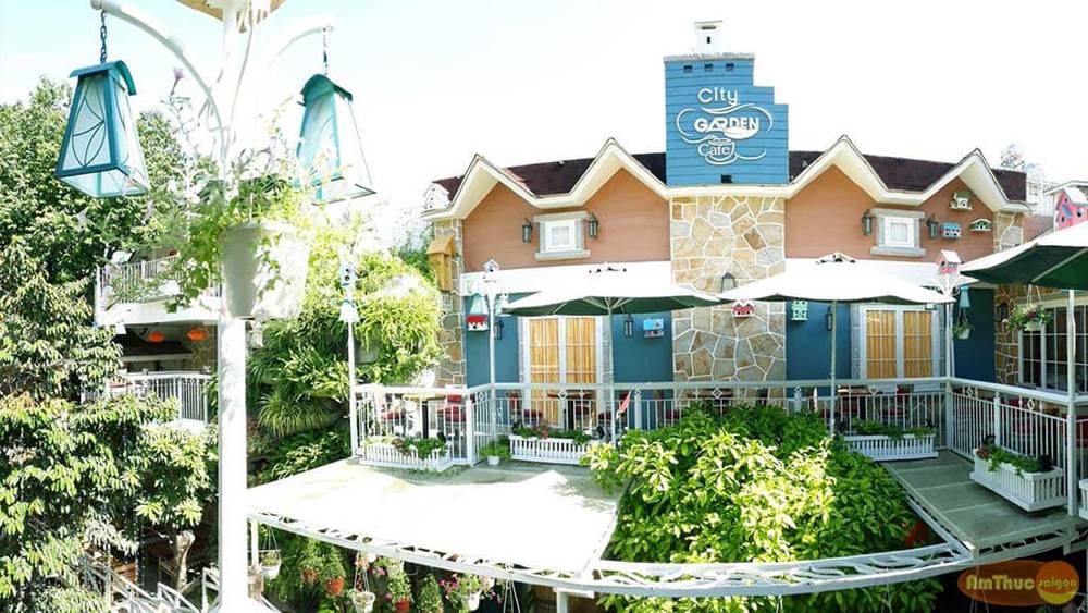 Qu&aacute;n c&agrave; ph&ecirc; với thiết kế nh&agrave; gỗ v&agrave; s&acirc;n vườn xanh m&aacute;t, c&oacute; m&aacute;i che v&agrave; đ&egrave;n trang tr&iacute;.