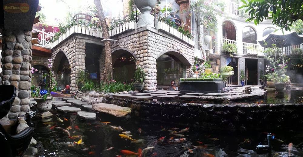 Hồ c&aacute; Koi trong khu&ocirc;n vi&ecirc;n với cầu đ&aacute; v&agrave; c&acirc;y xanh xung quanh, tạo kh&ocirc;ng gian y&ecirc;n b&igrave;nh v&agrave; thư gi&atilde;n.